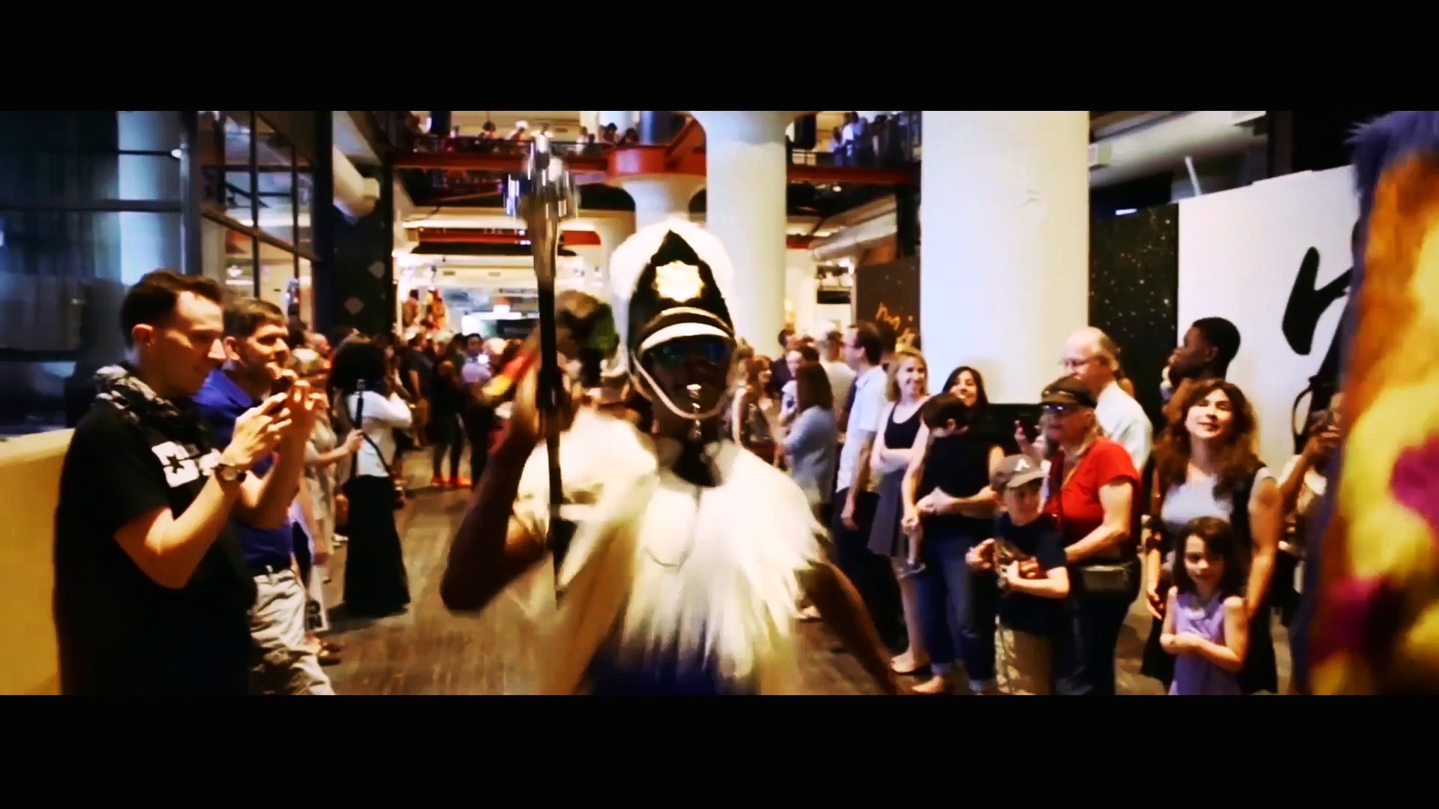 RikkiTheFool leading an indoor parade as a drum major before a crowd