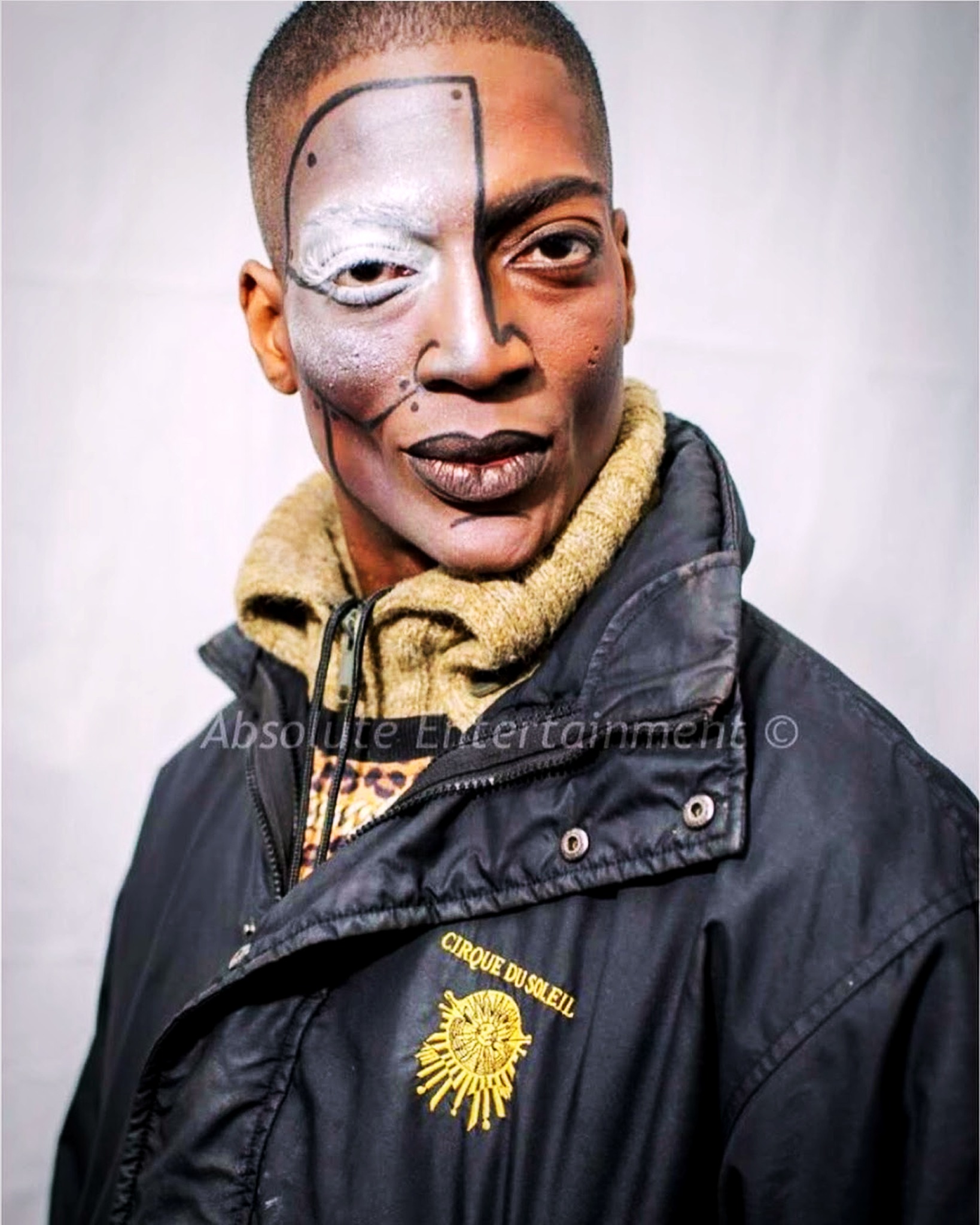 RikkiTheFool in half-face KURIOS makeup and a Cirque du Soleil jacket, with the original Absolute Entertainment watermark